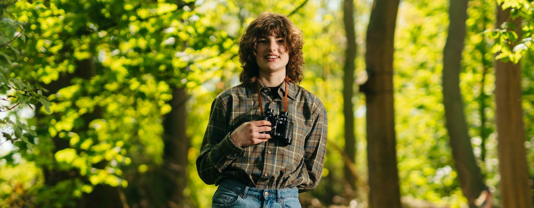 Country banner Countryside Management student with binoculars in woodland
